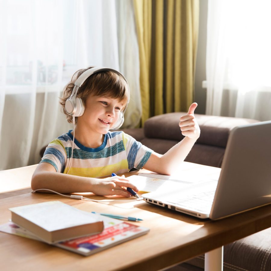 child boy  in headphones  show sight thumbs up, is using a lapto